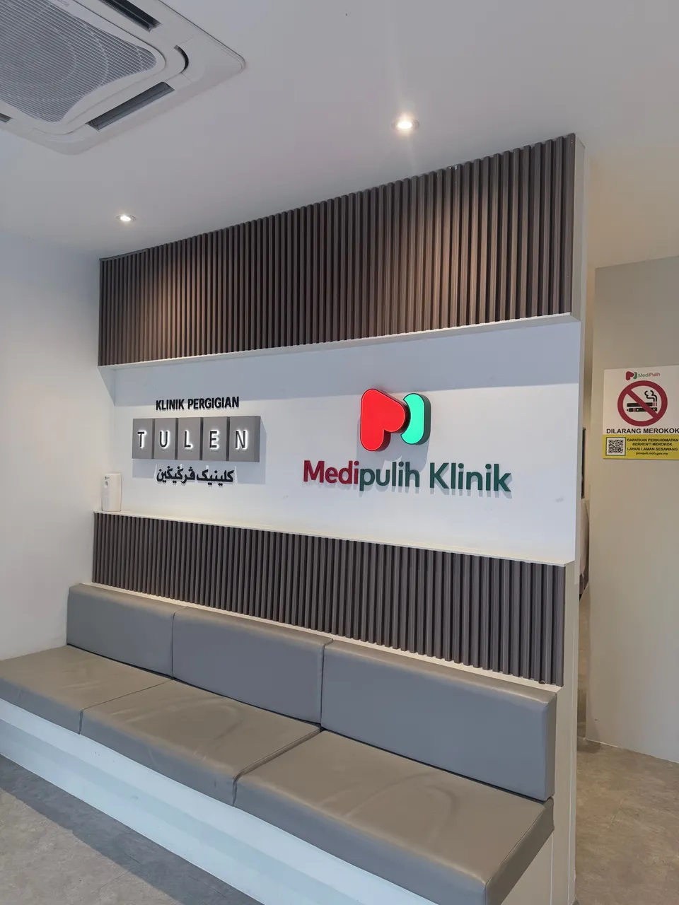 The waiting area at MediPulih Klinik's Kelana Jaya branch: grey bench seating below an illuminated MediPulih Klinik sign, beside the sign for Klinik Pergigian Tulen.