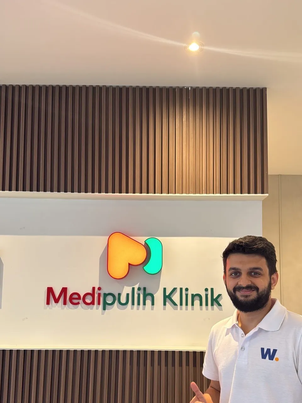 A member of the Watson team giving a thumbs up beside the illuminated MediPulih Klinik sign at one of the group's clinics.