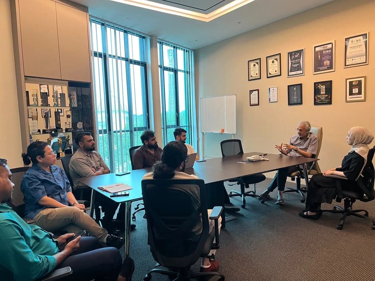 The Watson team in a meeting at AlShaik Group's headquarters, seated around a boardroom table with the group's awards framed on the wall behind.